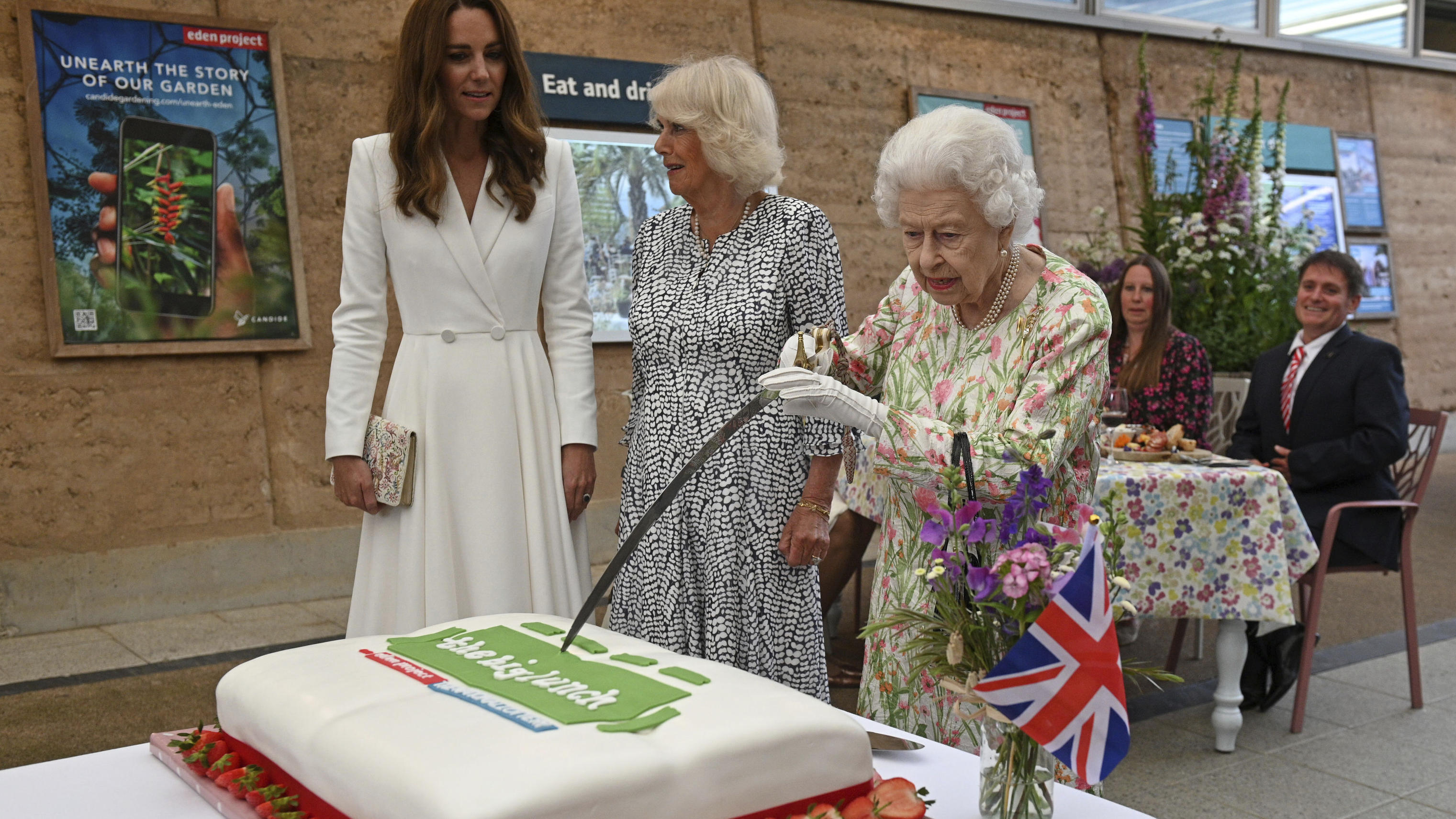 Die Queen mag Torte! Hier schneidet sie, neben Camilla und Kate, einen Kuchen mit einem Schwert an. Juni, 2021.