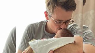 Dr. Johannes Wimmer hält ein Neugeborenes auf dem Arm und gibt ihm einen Kuss.