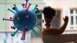 ARCHIV - 07.06.2021, Hessen, Frankfurt/Main: Ein stilisiertes Corona-Virus hängt in einem Schaufenster. Im Vordergrund ist eine Puppe zu sehen (zu dpa: «Inzidenz steigt kontinuierlich - Kommunen müssen Regeln verschärfen»). Foto: Sebastian Gollnow/dpa +++ dpa-Bildfunk +++
