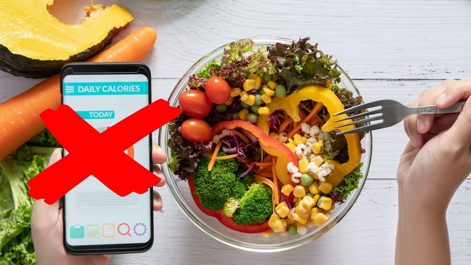 Eine Person schaut sich eine App zum Kalorienzählen auf ihrem Handy an, neben ihr steht ein großer Salat.