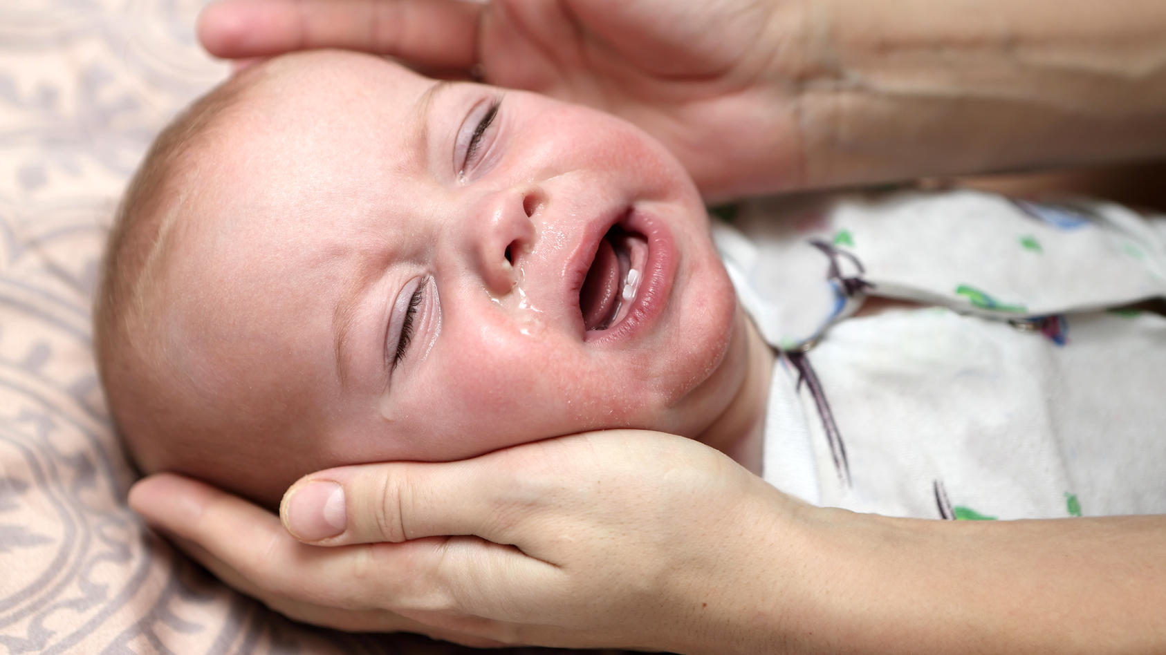 Ein krankes Baby mit Schnupfennase liegt in seinem Bettchen und weint.
