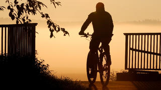 03.09.2021, Baden-Württemberg, Riedlingen: Ein Radfahrer fährt am Morgen im Gegenlicht der Sonne über eine Brücke. Foto: Thomas Warnack/dpa +++ dpa-Bildfunk +++