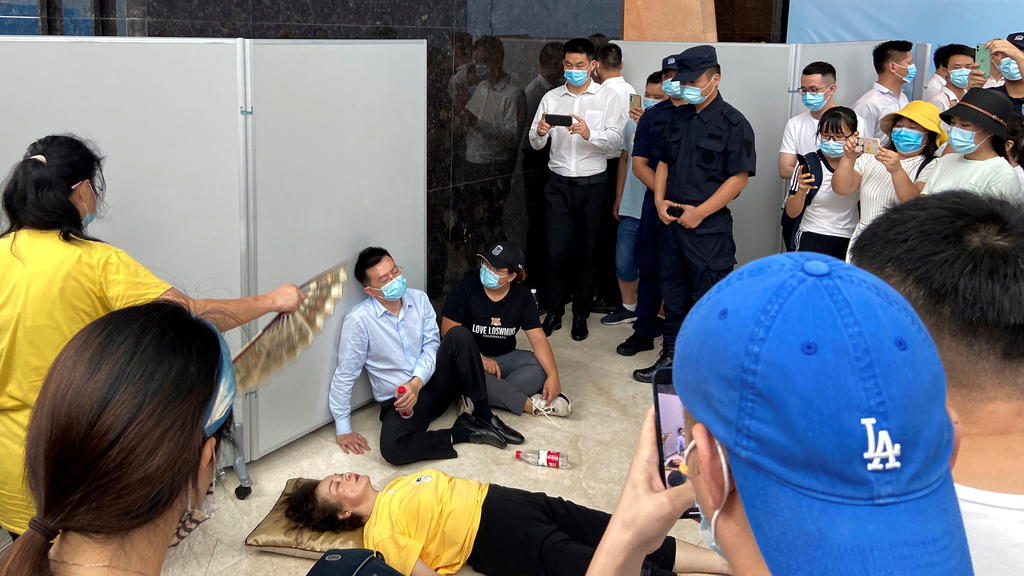 A woman receives aid on the ground next to Du Liang, general manager and legal representative of Evergrande's wealth management division, while people gather to demand repayment of loans and financial products at the Evergrande's headquarters, in She