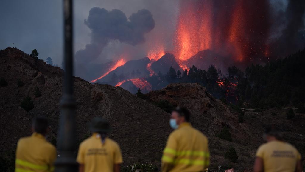 19.09.2021, Spanien, La Palma: Feuerwehrmänner beobachten den Vulkan Cumbre Vieja auf der kanarischen Insel La Palma. Der Ausbruch hatte sich in den vergangenen Tagen durch Tausende kleine Erdbeben und eine leichte Anhebung des Erdbodens angekündigt.
