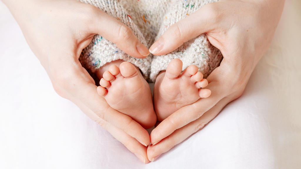 Eine Mutter hält die Füße ihres Babys in der Hand und formt ihre Hände zu einem Herz.