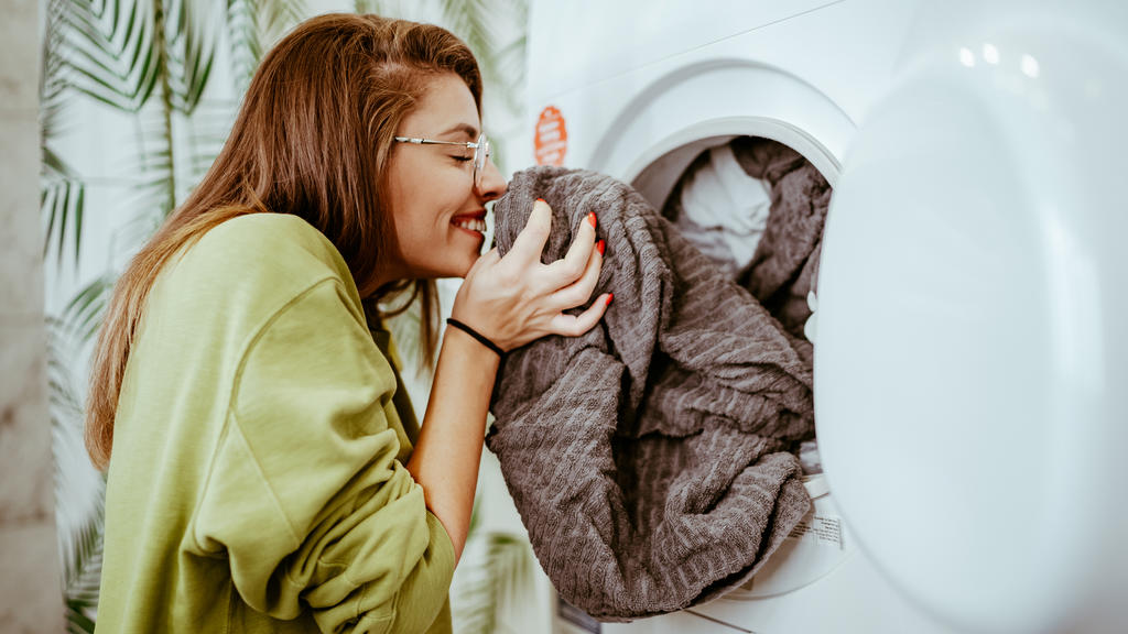Eine junge Frau mit Brille riecht an ihrer frisch gewaschenen Wäsche.