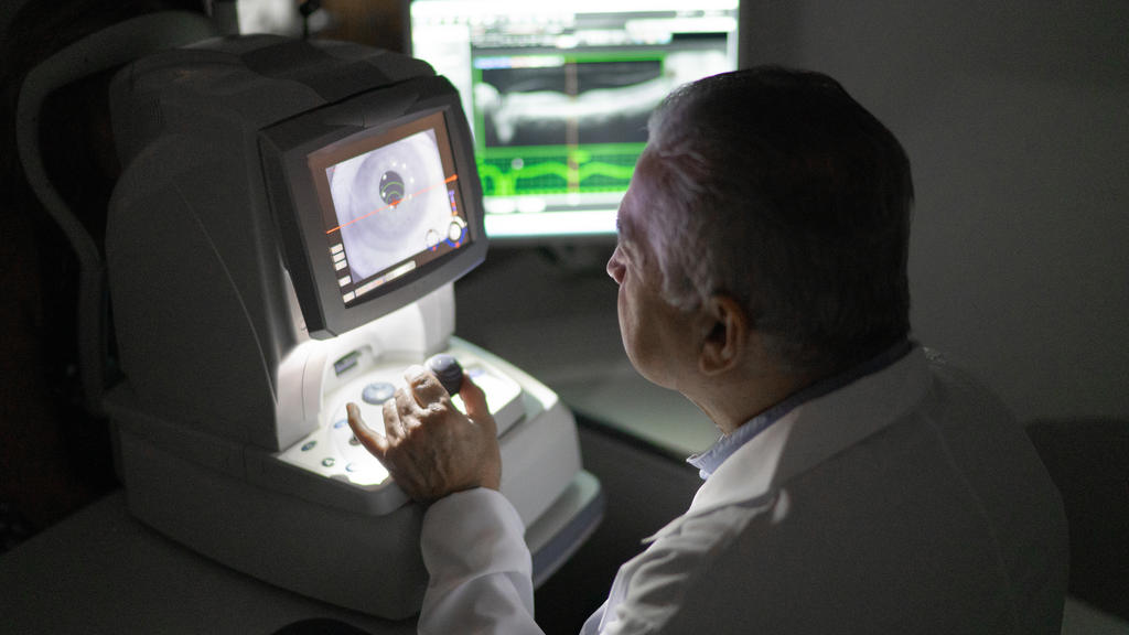 Ein Augenarzt bzw. Optiker schaut sich auf einem technischen Gerät ein vergrößertes Auge an.
