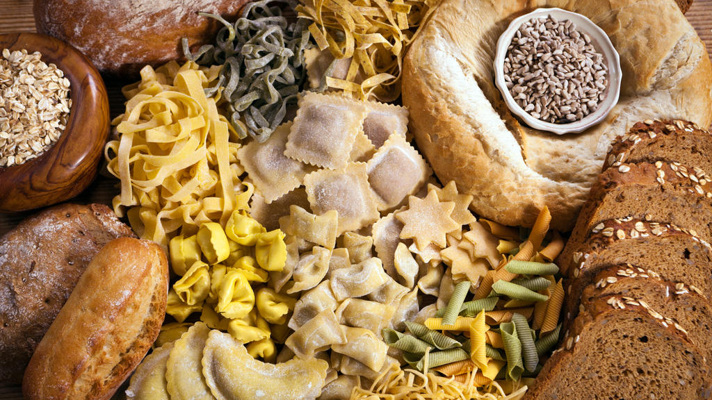 Verschiedene, kohlenhydratreiche Lebensmittel, wie Pasta, Brot und Co. liegen auf einem Tisch.