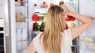Frau steht ratlos vor dem offenen Kühlschrank