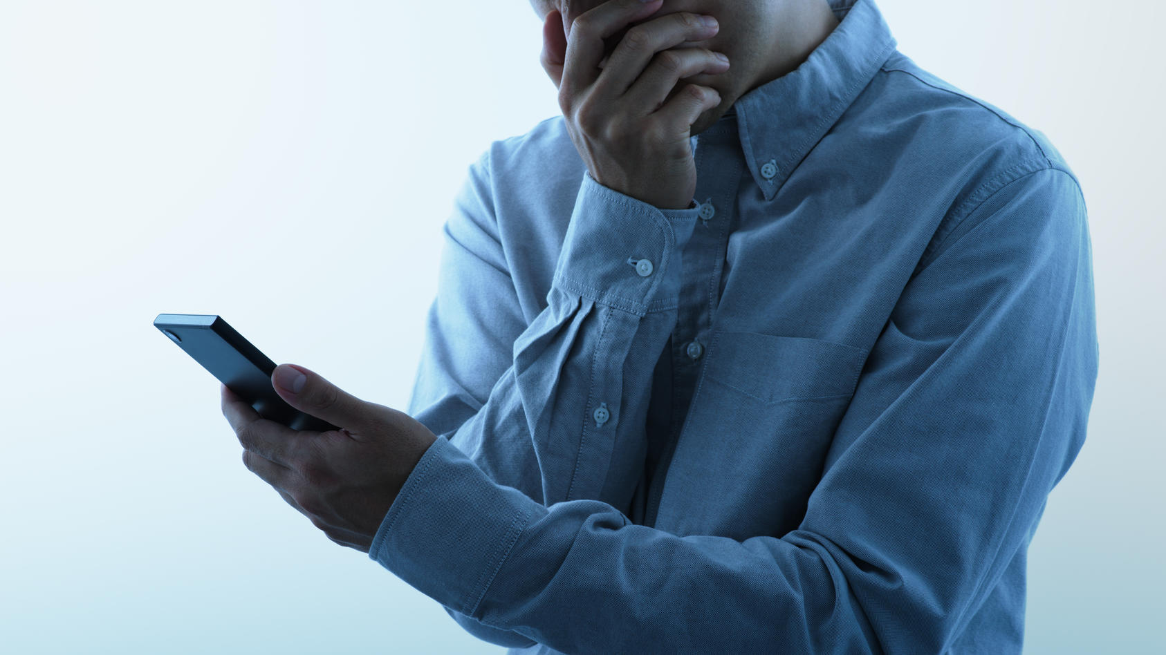 Ein Mann schaut entsetzt auf sein Handy, vermutlich wurde er Opfer einer Betrugsmasche per Telefon.