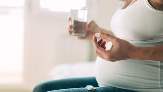 Eine schwangere Frau sitzt auf dem Sofa und nimmt ihre Medikamente.