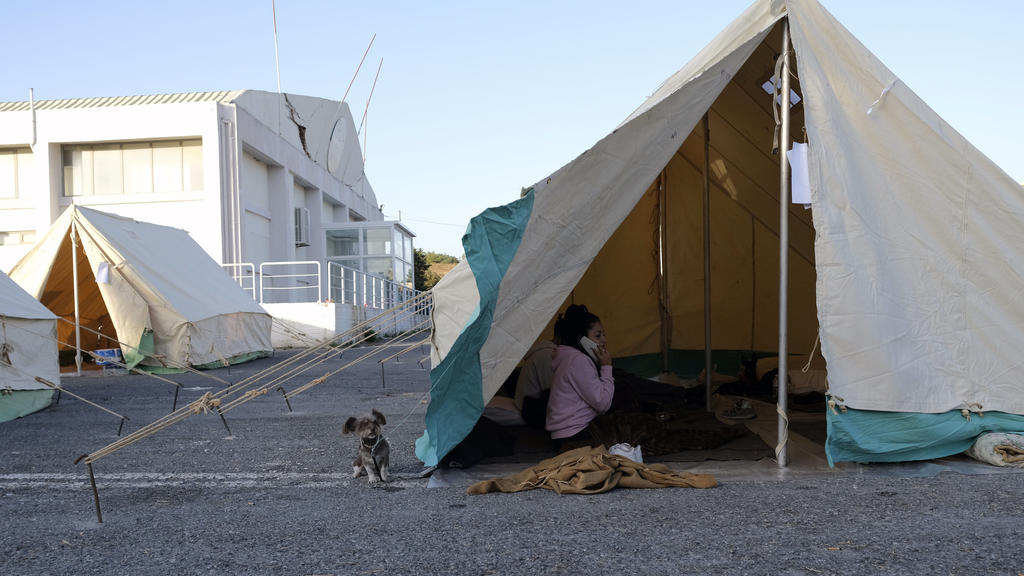 28.09.2021, Griechenland, Arkalochori: Eine Frau telefoniert mit ihrem Handy, während ein Hund vor einem Zelt im Dorf Arkalochori auf der südlichen Insel Kreta steht. Erneut hat ein Beben am Dienstagmorgen die Mittelmeerinsel Kreta erschüttert. Foto: