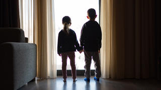 Zwei Kinder stehen händchenhaltend vor einem Fenster.