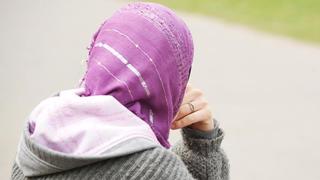 Eine junge Frau mit Kopftuch sitzt an einem Weg