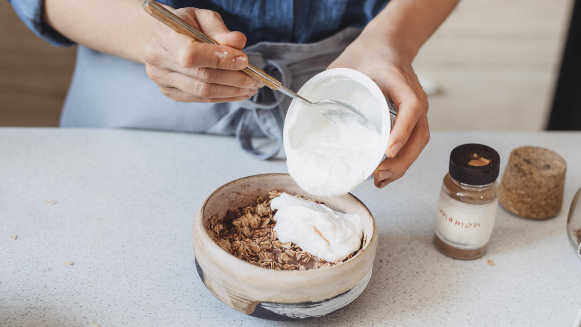 Frau bereitet Müsli mit veganem Joghurt zu