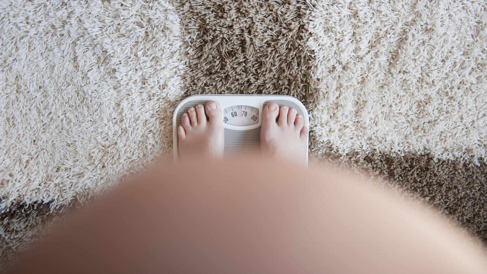 Eine schwangere Frau steht auf einer Waage und begutachtet ihr Gewicht.