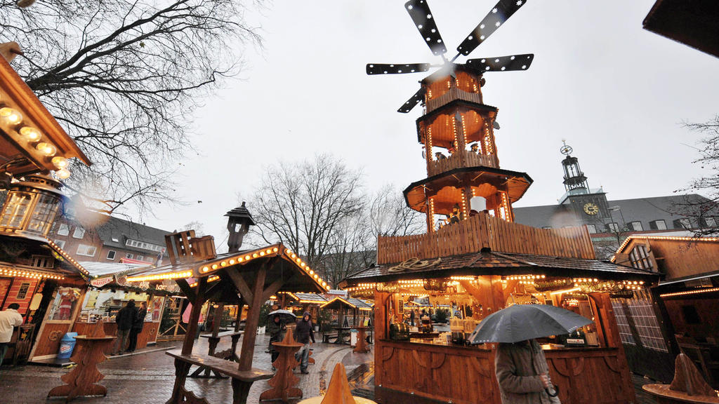 Mit einem Regenschirm geschützt geht am Dienstag (23.11.2010) eine Frau bei strömenden Regen über den neu gestalteten Weihnachtsmarkt in Emden an der zum ersten mal aufgestellten 12 Meter hohen Holzpyramide vorbei. Foto: Carmen Jaspersen dpa/lni +++