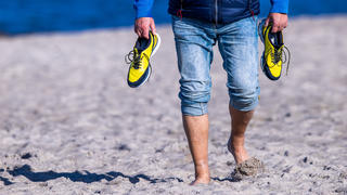 Ein Urlauber geht bei Sonnenschein barfuß am Strand auf der Ostseeinsel Poel spazieren. Sonnig und mit Temperaturen um die 15 Grad zeigt sich das Herbstwetter in Norddeutschland von seiner freundlichen Seite.