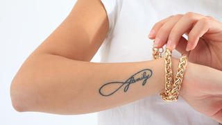 Eine Frau trägt ein dezentes "Infinity"-Symbol-Tattoo auf dem Arm.