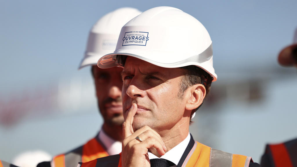 French President Emmanuel Macron, wearing a working helmet, listens to workers as he visits the building site of the Olympic Village as part of a visit to construction sites dedicated to Paris 2024 Olympic and Paralympic Games, in Paris suburb Saint-