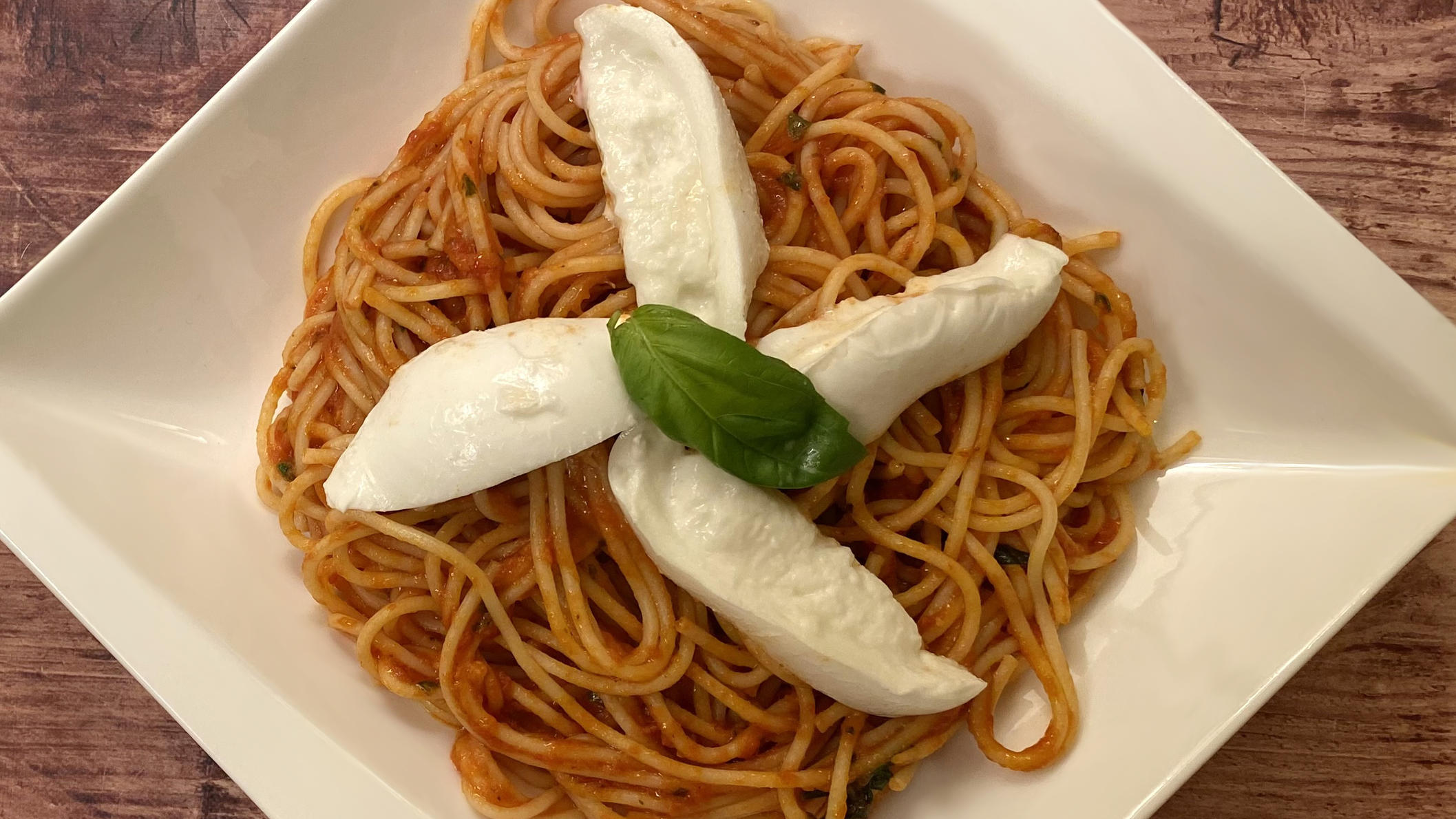 Auf einem Teller sind Spaghetti in einer Tomate-Mozzarella-Soße auf einem Teller angerichtet.