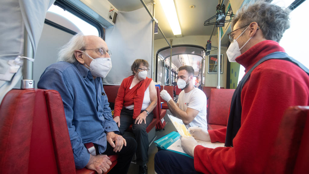 04.11.2021, Hessen, Frankfurt/Main: Eine Frau lässt sich in der ·Impftram· in Frankfurt eine Booster-Impfung gegen Corona spritzen, während ihr Ehemann mit dem Arzt spricht. Impfwillige können ohne Termin jederzeit in die Bahn einsteigen, die auf reg