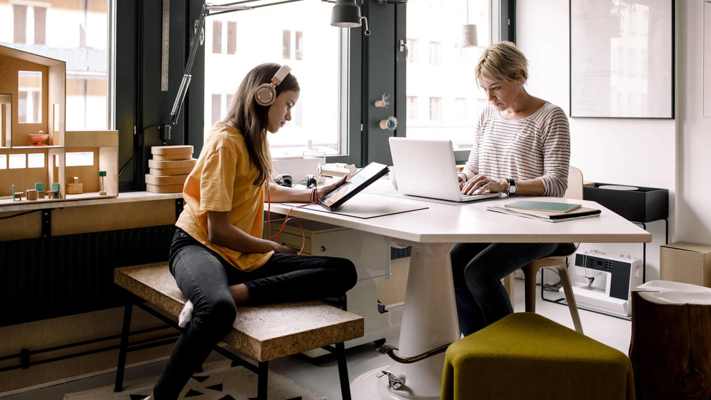 Frau im Homeoffice, Tochter sitzt mit Tablet mit am Tisch