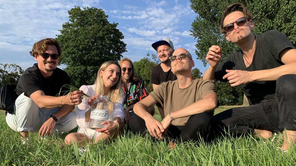 Die Musiker der kölschen Band Cat Ballou sitzen gemeinsam mit RTL-Reporterin Daria auf einer grünen Wiese.