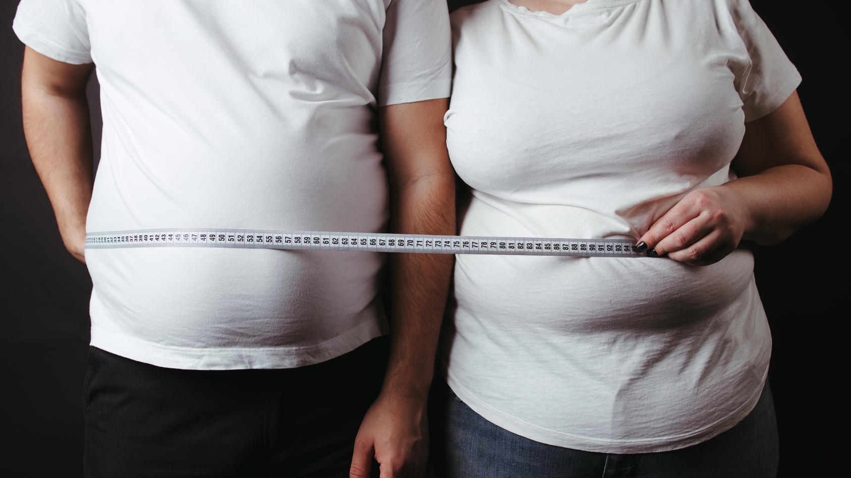 Ein übergewichtiger Mann und eine ebenso übergewichtige Frau posieren für die Kamera mit einem Maßband.