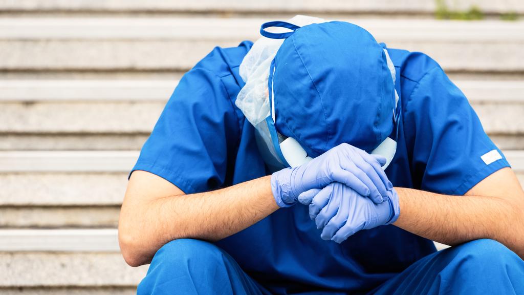 Ein Arbeiter aus dem Gesundheitsbereich hält den Kopf gesenkt und wirkt verzweifelt.
