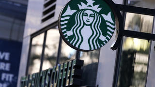 The "Siren" logo hangs outside a Starbucks Coffee shop, Wednesday, July 14, 2021, in Boston. Starbucks said Wednesday, Oct. 27 it is raising its U.S. employeesâ€™ pay and making other changes to improve working conditions in its stores.  (AP Photo/Charles Krupa)