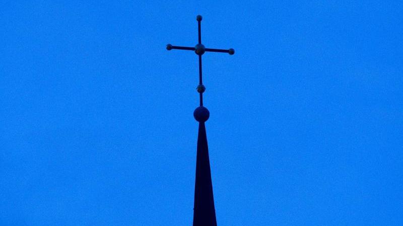 Das Kreuz einer Kirche ist in der Abenddämmerung zu sehen. Foto: Friso Gentsch/dpa/Symbolbild