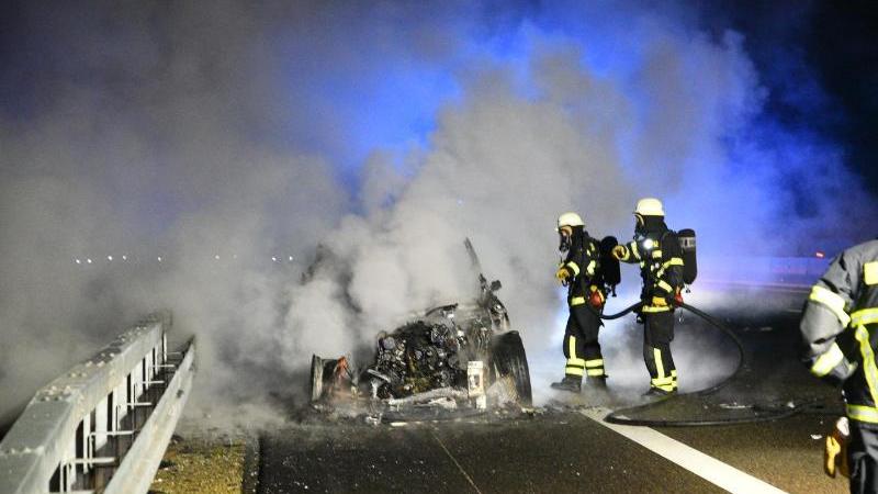 Feuerwehrleute versuchen am Samstagabend ein brennendes Fahrzeug auf der A6 zu löschen. Foto: Priebe/dpa