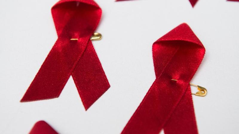 Rote Schleifen, das Symbol für die Solidarität mit HIV-Infizierten, liegen auf einem Tisch. Foto: Lukas Schulze/dpa/Symbolbild