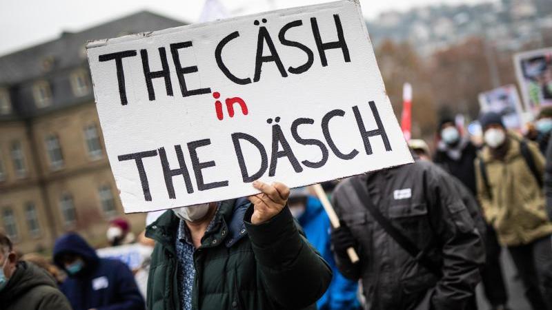 "The Cäsh in The Däsch" steht bei einer Kundgebung auf dem Schild eines Teilnehmers geschrieben. Foto: Christoph Schmidt/dpa/Archivbild