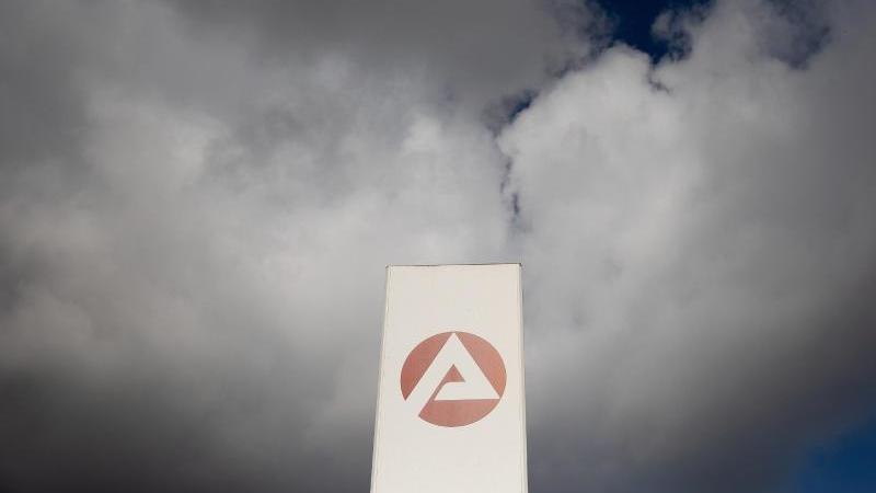 Wolken ziehen über ein Schild der Agentur für Arbeit. Foto: Carsten Koall/dpa/Bildarchiv