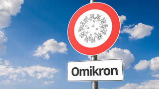 Verkehrsschild mit Omikron-Aufschrift und Coronavirus-Symbol