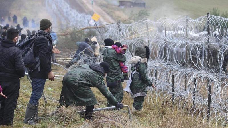 Migranten, die an der weißrussisch-polnischen Grenze einen Zaun umstoßen, während die Polizei hinter einem Stacheldrahtzaun steht. Foto: Leonid Shcheglov/BelTA/AP/dpa