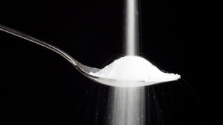 Sugar being poured on a spoon isolated on a black background