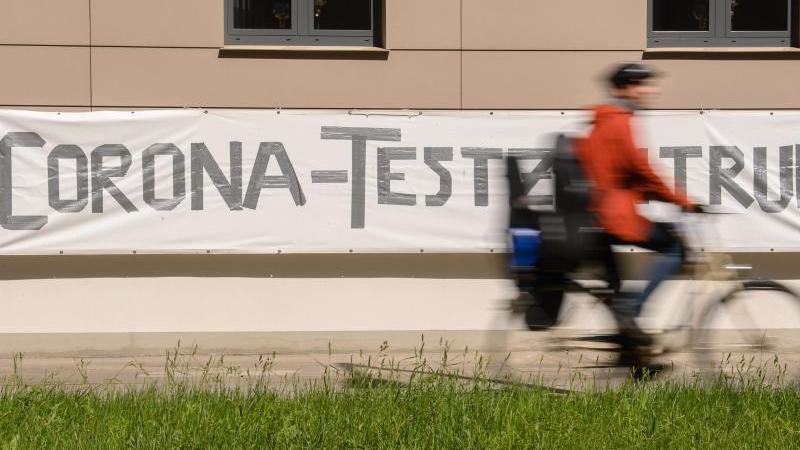 Ein Radfahrer fährt an einem Banner mit der Aufschrift "Corona-Testzentrum" vorbei. Foto: Robert Michael/dpa-Zentralbild/dpa/Symbolbild