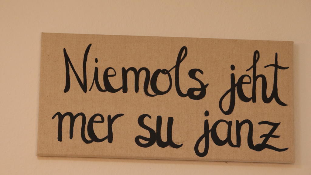 Auf einem Schild steht in geschwungenen Lettern "Niemols jeht mer su janz"