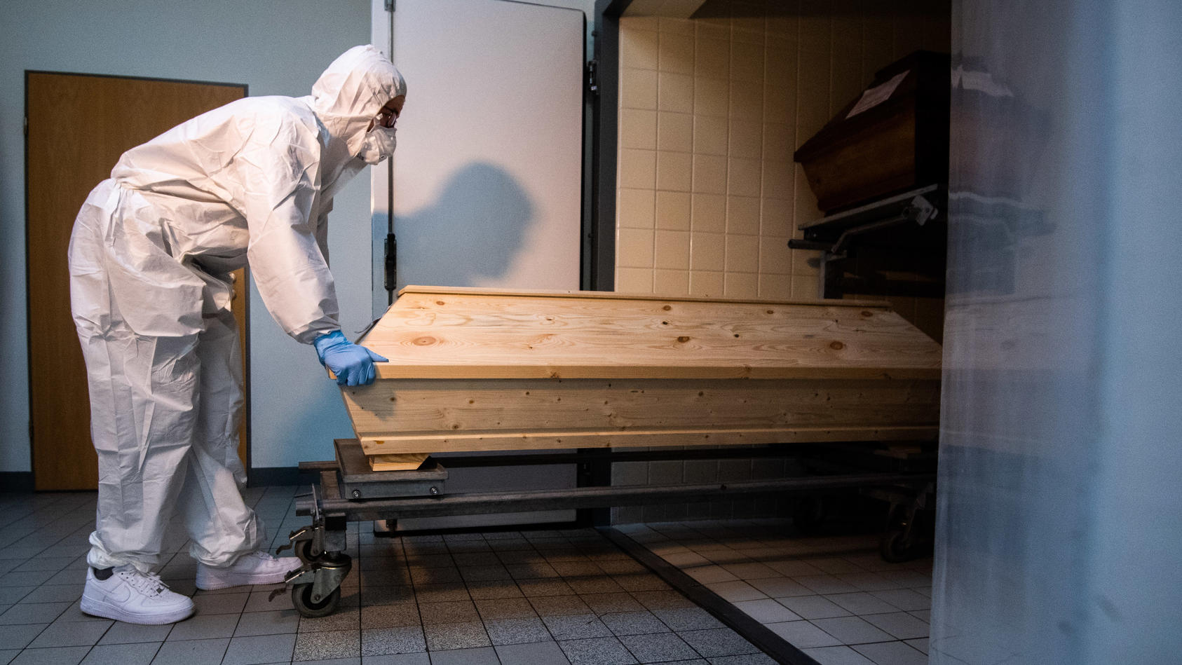 Ein Krematorium-Mitarbeiter zieht vermummt einen Sarg aus einem Schrank. 
