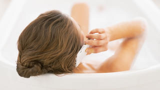 Young woman talking cell phone while in bathtub. rear view