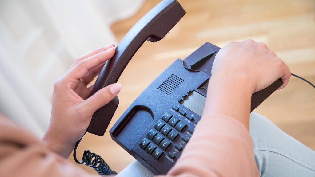 Eine junge Frau nimmt in einer Wohnung ein Festnetz-Telefon in die Hand.