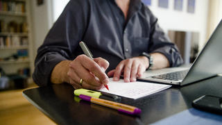 ARCHIV - 01.10.2021, Bayern, München: Ein Mann sitzt zuhause an einem Esstisch. Er schreibt mit einem Stift auf ein Blatt Papier neben einem Laptop. (Gestellte Szene)Die pandemiebedingte Umstellung auf die Arbeit aus dem Homeoffice hat sich einer Untersuchung des Nürnberger Instituts für Arbeitsmarkt- und Berufsforschung (IAB) zufolge bewährt. (zu dpa "Umfrage: Homeoffice hat sich als Schutzmaßnahme bewährt") Foto: Finn Winkler/dpa +++ dpa-Bildfunk +++