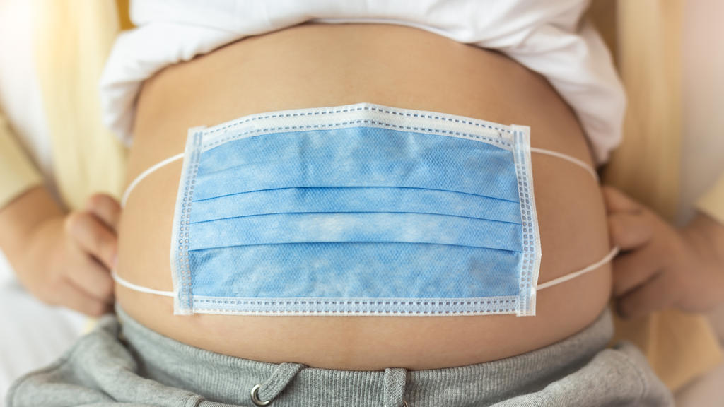 Schwangere mit OP-Maske auf dem Bauch