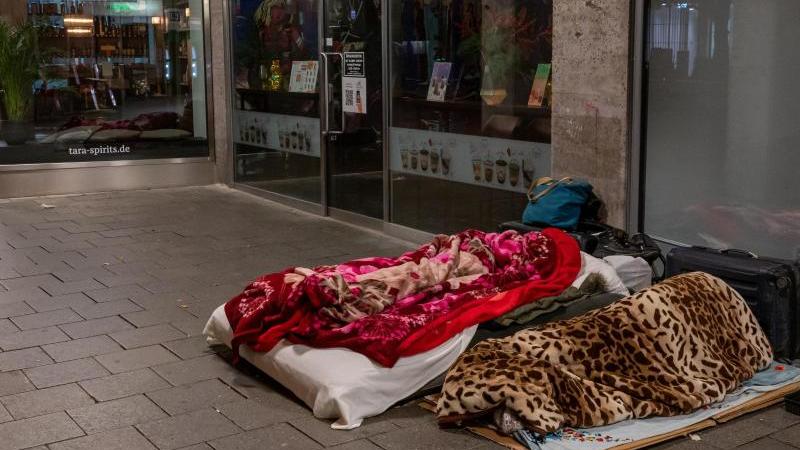 Zwei Obdachlose schlafen vor der überdachten Fassade einer Ladenpassage. Foto: Peter Kneffel/dpa