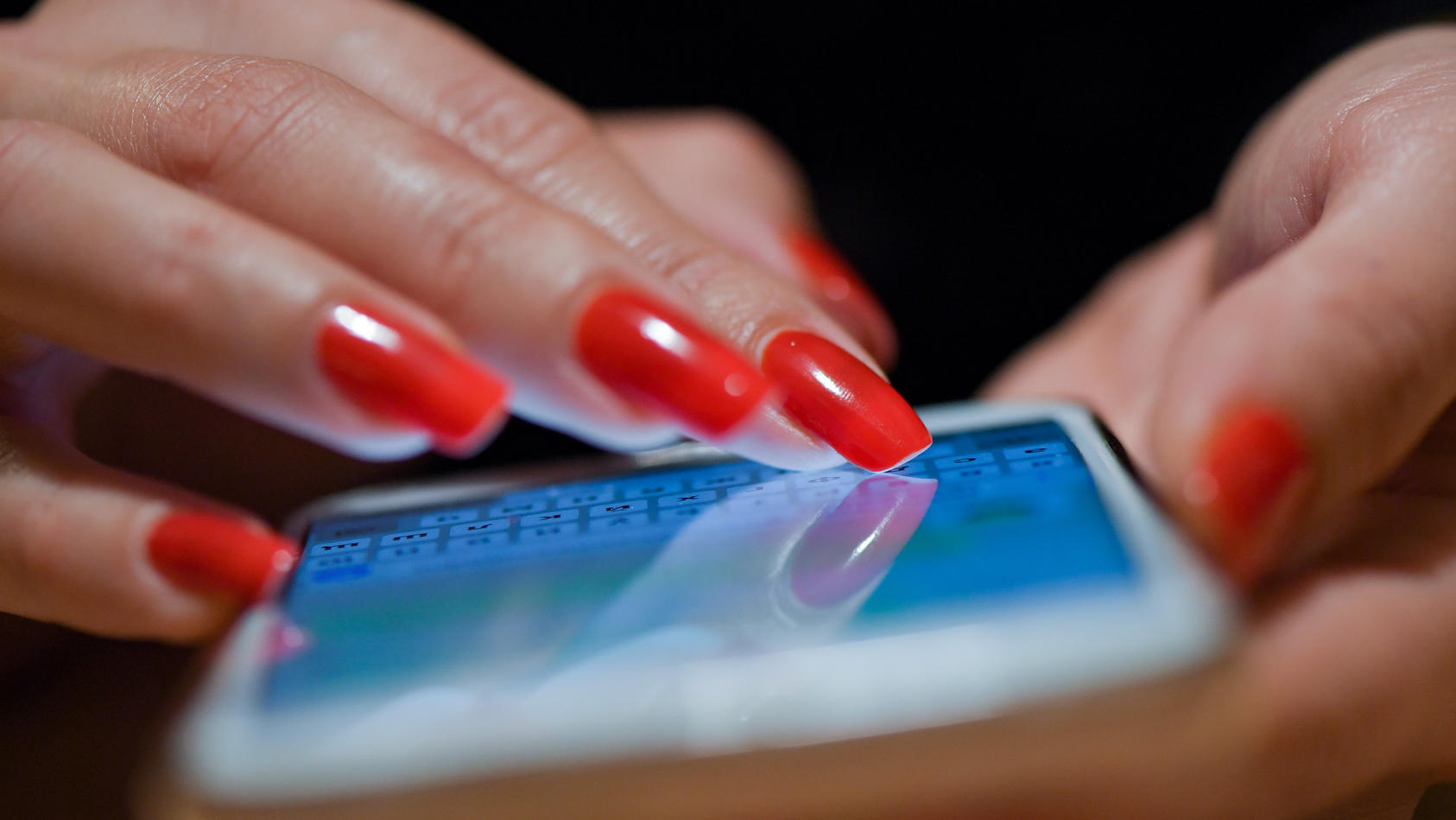 ARCHIV - 08.11.2019, Brandenburg, Sieversdorf: Eine Frau mit roten Fingernägeln schreibt eine Nachricht auf ihrem Smartphone. In Lockdown-Zeiten boomten Online-Dating-Plattformen noch mehr als zuvor - und das wird aus Sicht von Experten auch nach der