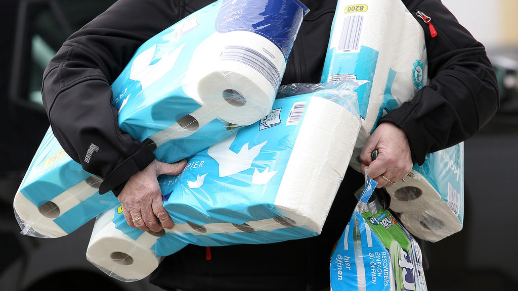 Ein Mann trägt eingekauftes Toilettenpapier und Küchenrollen aus einem Supermarkt.