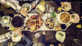Family having traditional holiday dinner with stuffed turkey, mashed potatoes, cranberry sauce, vegetables pumpkin and pecan pie.